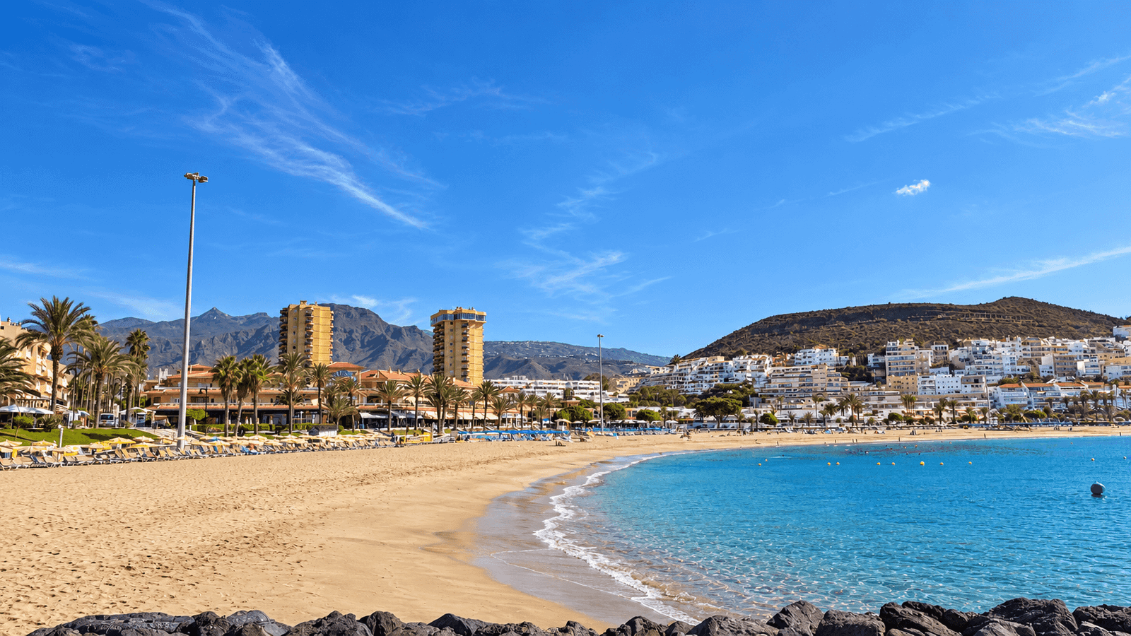 Sandy beach in Playa de Las Américas, Tenerife with clear water and mountains in the background